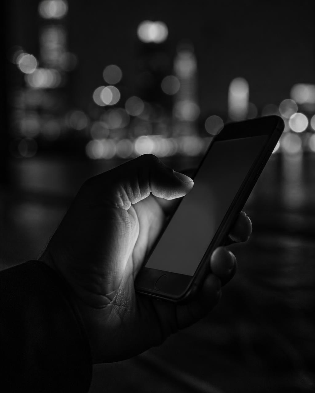 Hand holding a smartphone at night with city lights blurred behind